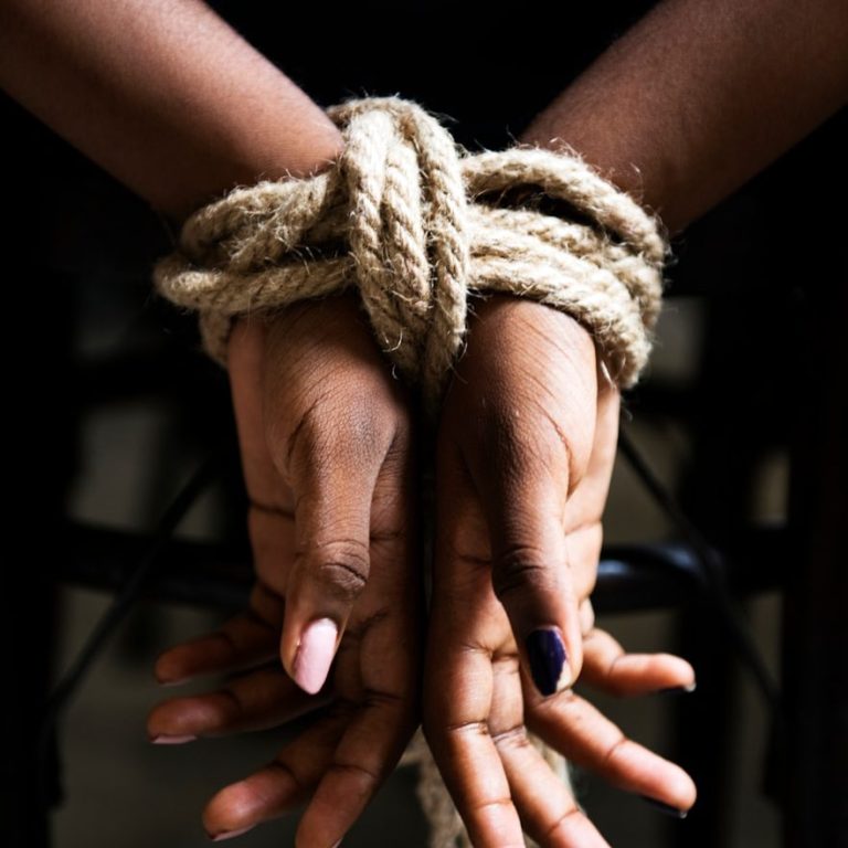Hände mit Seil gefesselt, auf einem dunklen Hintergrund.
